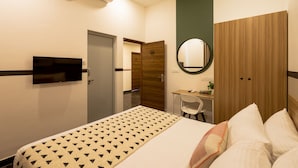 Habitación de hotel con cama, escritorio con silla, televisión, armario y unidad de aire acondicionado.