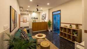Zona de recepción de un hotel con mostrador, un sofá verde, una mesita redonda y una estantería.