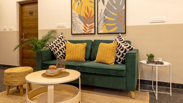 Un sofá verde con cojines estampados, una mesita redonda con una vela y una planta en maceta.