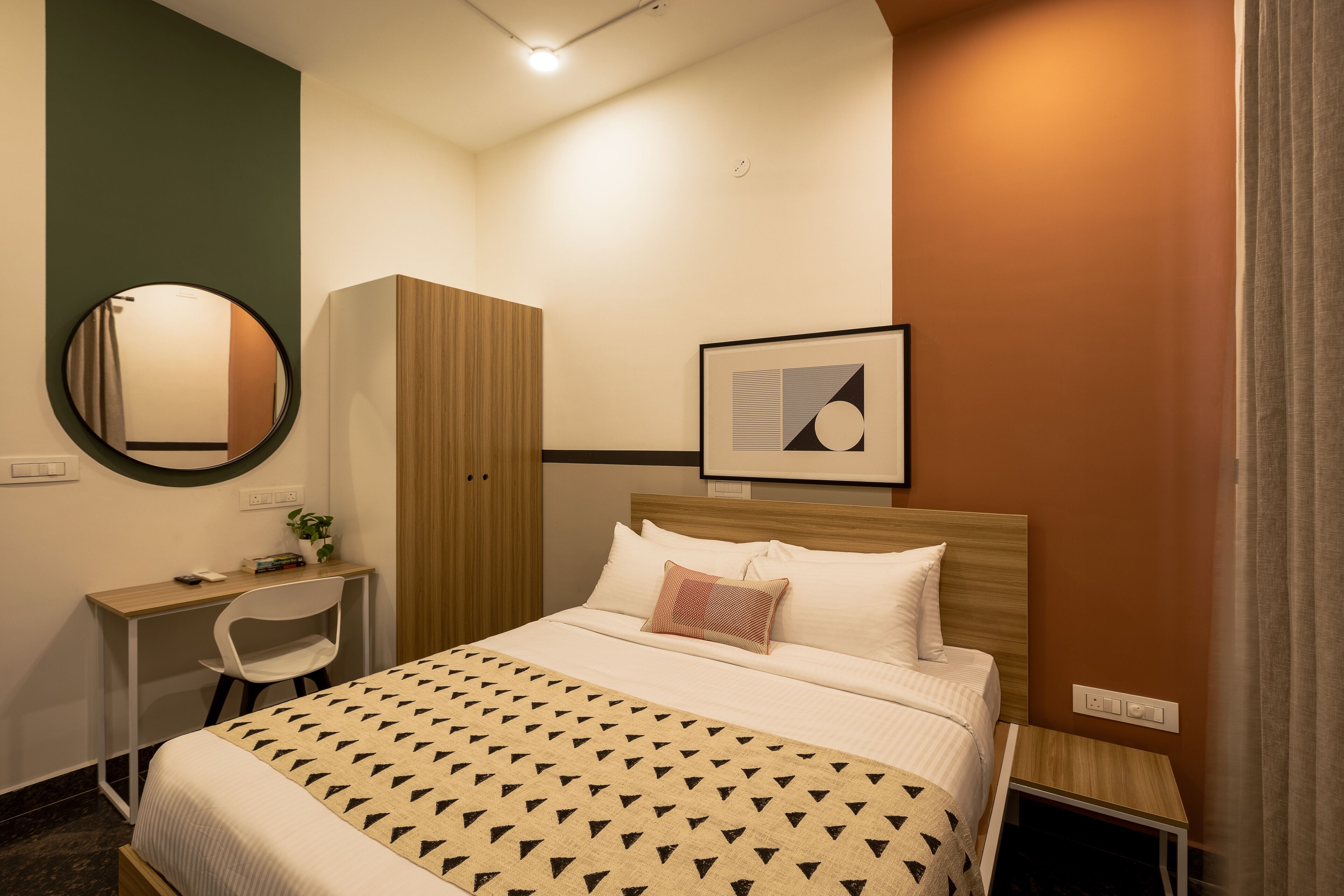 Een keurig opgeruimde hotelkamer met een bed, een bureau met stoel, een kledingkast en een lijst aan de muur.