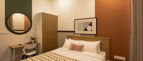 A neatly arranged hotel room with a bed, a desk with a chair, a wardrobe, and a framed picture on the wall.