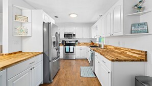 A modern kitchen with white cabinets, a wooden countertop, stainless steel appliances, and decorative signs on the walls.