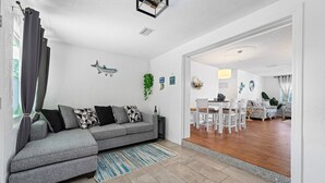A modern living room with a grey sectional sofa, a blue striped rug, and a dining area with white chairs and a table.
