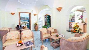 Ein großzügiger Lounge-Bereich mit Rattanmöbeln, Meerblick und einer Rezeption mit Blumenarrangement.