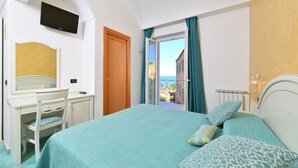 Ein Schlafzimmer mit Bett, Schreibtisch, Stuhl, einem an der Wand montierten Fernseher und einem Balkon mit Meerblick.