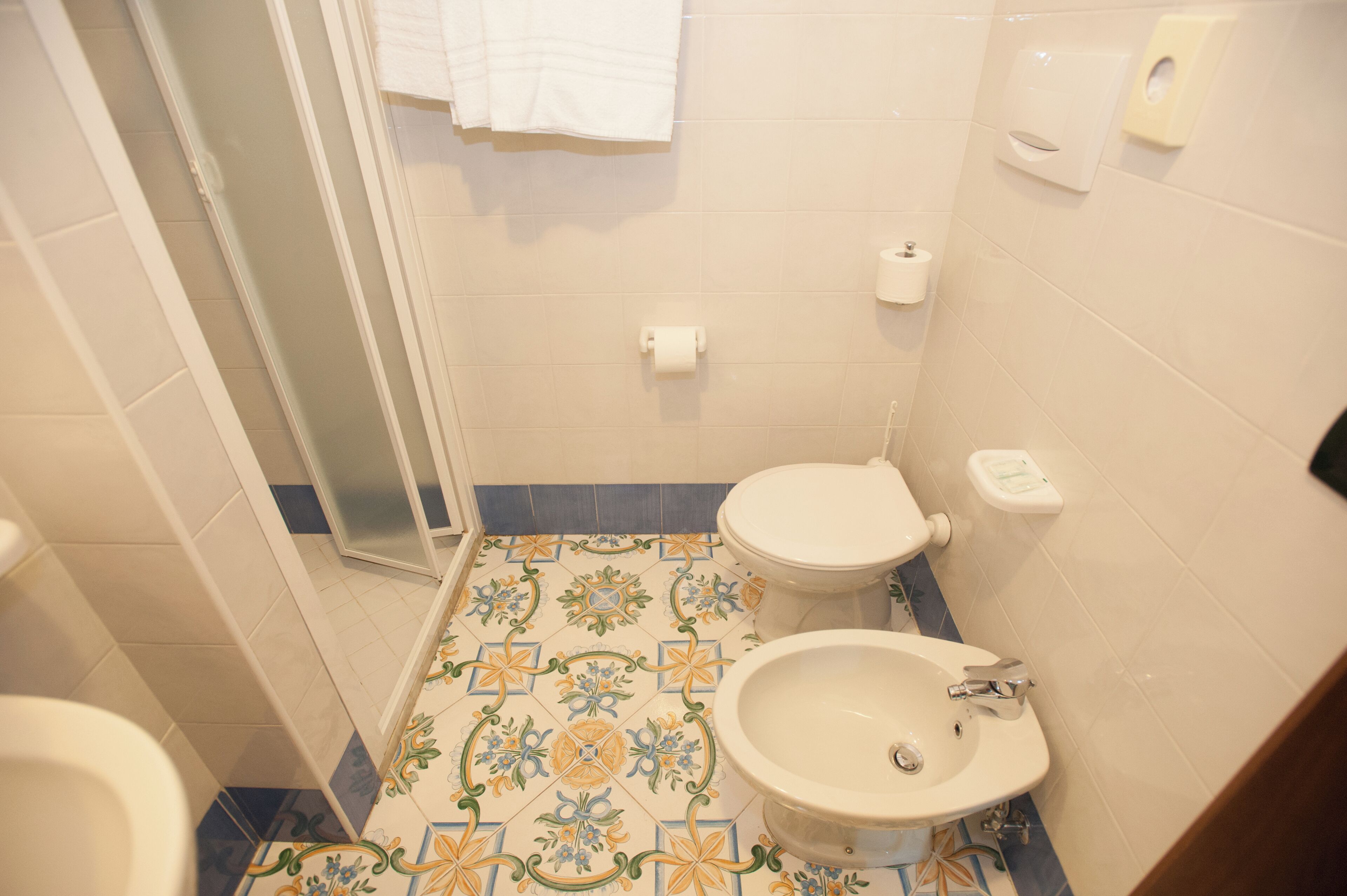 Un baño con ducha, inodoro y lavamanos, con baldosas de diseño en el suelo y paredes blancas.
