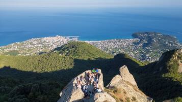 A group of people on a rocky outcrop overlooking a coastal town with a bridge in the distance.