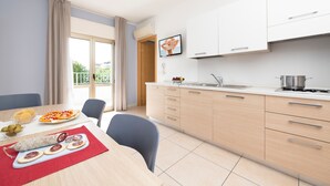 A modern kitchen with light wood cabinets, a sink, and a dining area with a table set for two. - Residence Quadrifoglio (Cervia)