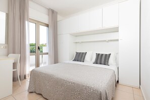 A bedroom with a bed, a desk, and a window with curtains. - Residence Quadrifoglio (Cervia)