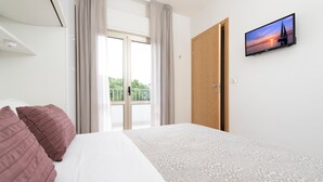 A hotel room with a bed, a television on the wall, and a view of the outdoors through a window. - Residence Quadrifoglio (Cervia)