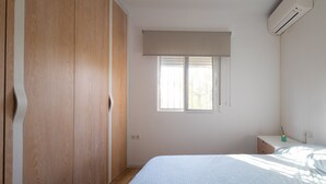 A bedroom with a bed, a wardrobe, a window with blinds, and an air conditioning unit.
