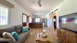 A spacious living area with a sofa, a wooden coffee table, a TV, and a kitchen in the background.