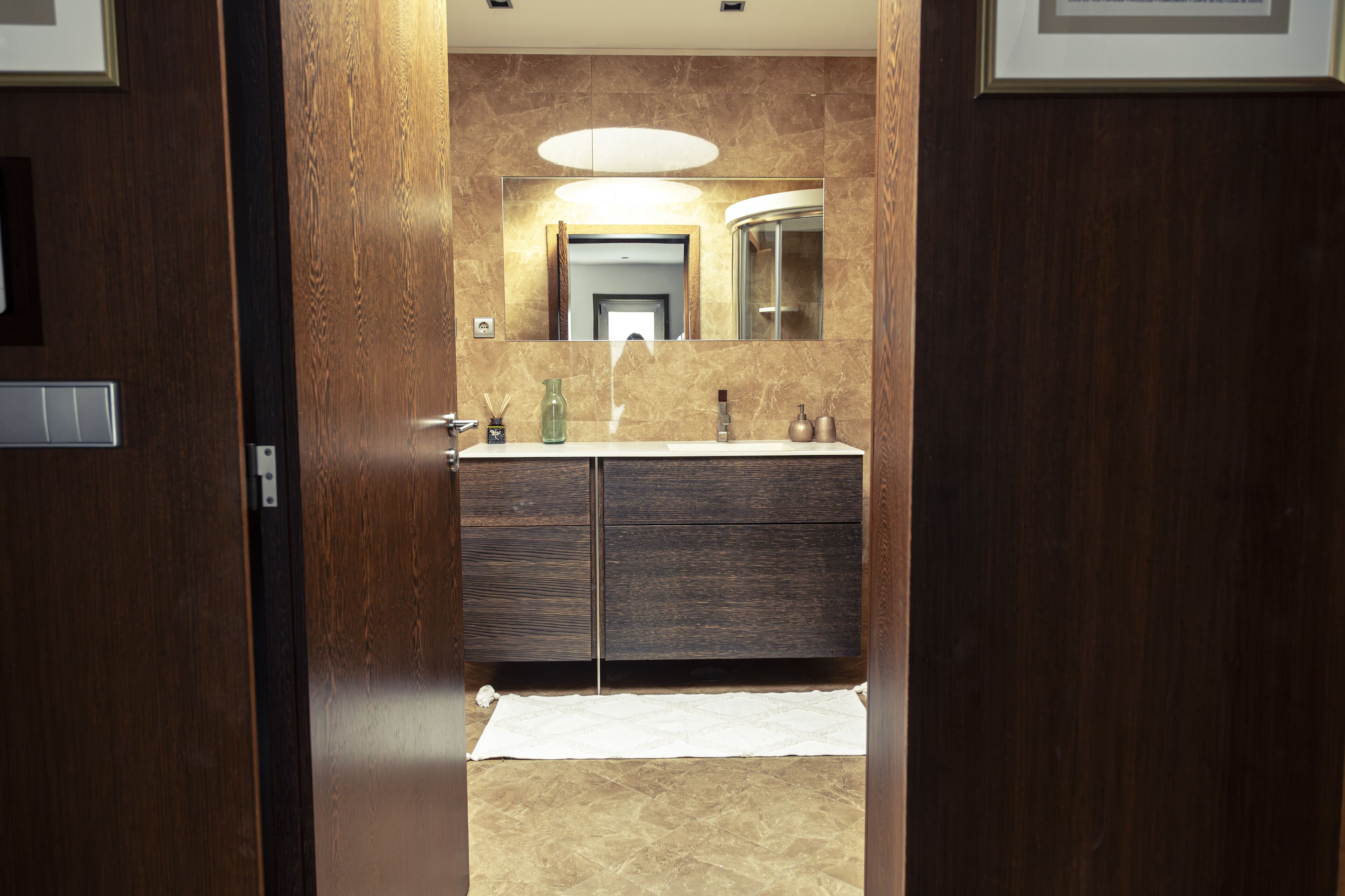 A bathroom with a wooden vanity, a large mirror, and a white towel on the floor.