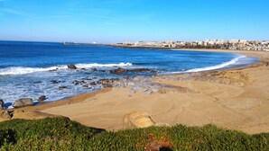 Une plage côtière aux eaux d’un bleu limpide, avec un rivage sablonneux et une vue lointaine sur la ville.