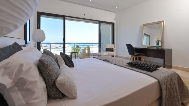 A modern bedroom with a large bed, a desk, and a view of the sea through large windows. - Villa Tanit  (La Marsa)