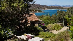 A garden with two lounge chairs, a stone building with a tiled roof, and a view of a coastal area with mountains in the background. - VILLA LILIUM (Punta Molara)