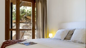 A bedroom with a bed, a window with curtains, and a lamp on the nightstand. - VILLA LILIUM (Punta Molara)