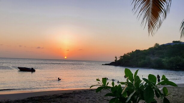 A beach scene with a boat on calm water, a person swimming, and a person walking along the shore. - New construction spacious villa with beautiful sunset view quick ride to beach!  (Fountain, Saint Vincent and The Grenadines)
