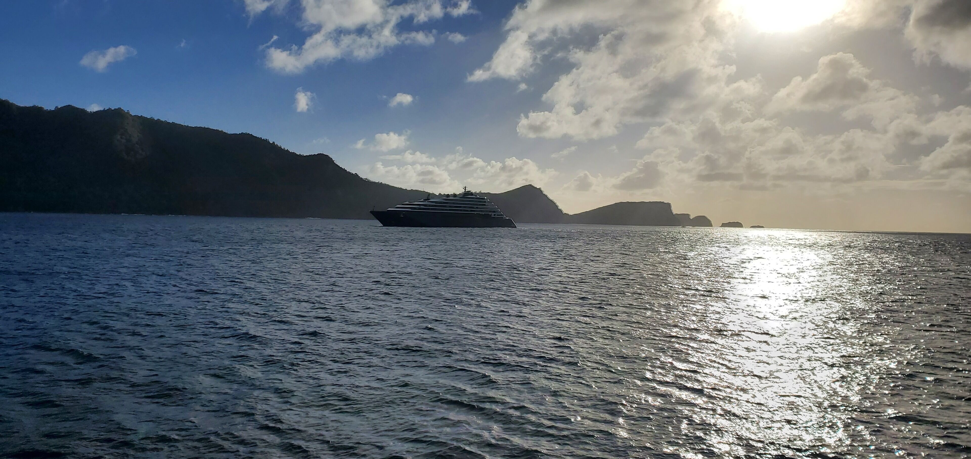 A cruise ship on a calm sea with mountains in the background.