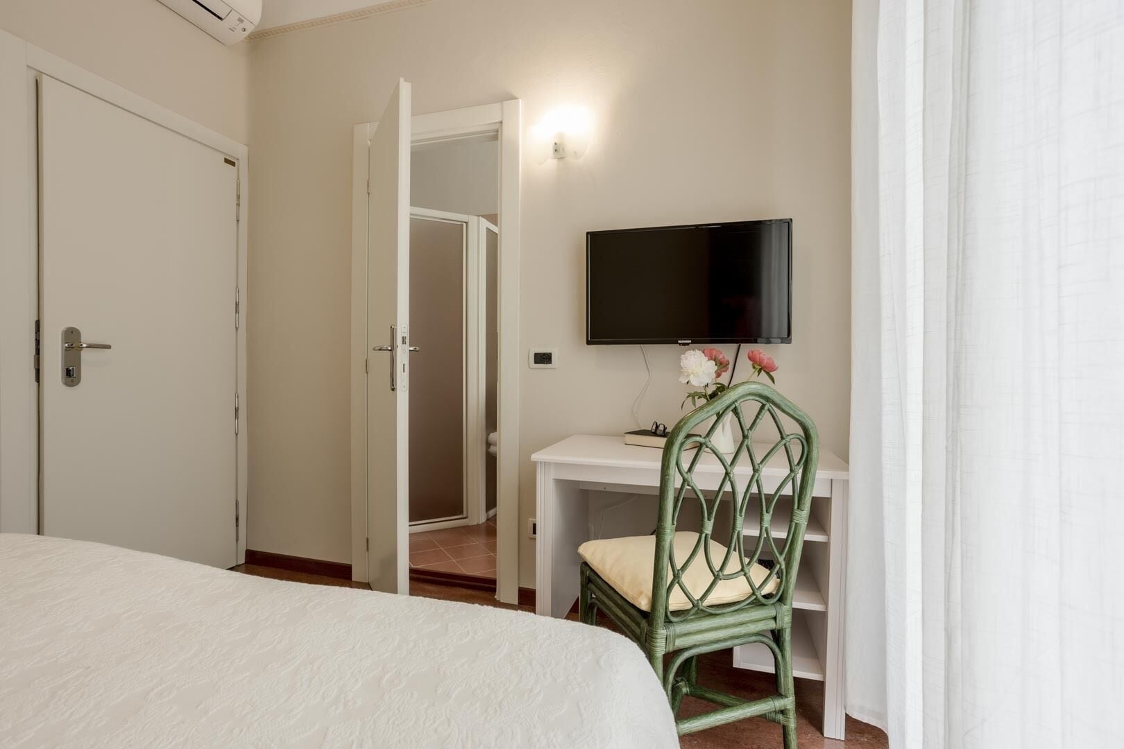 A hotel room with a bed, a desk with a chair, a television, and a door.