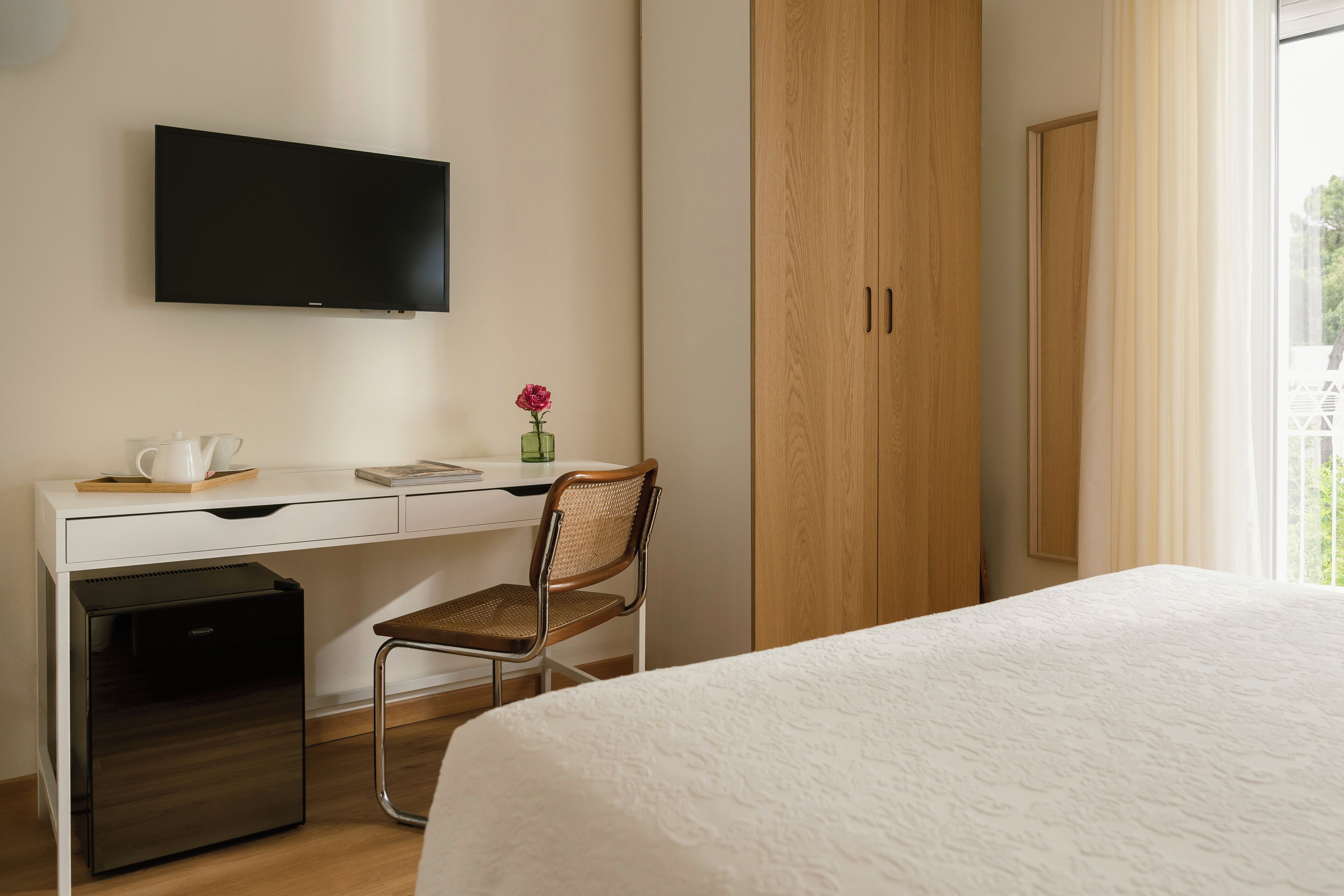 Habitación de hotel con cama, escritorio con televisor, refrigerador pequeño, silla y armario.