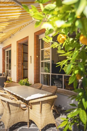 An outdoor patio with wicker furniture, a table, and a covered area with a striped awning. - Villa Arizona B&B (Cervia)