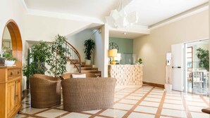 A spacious living area with a checkered floor, a wooden cabinet, wicker furniture, and a staircase leading to another room. - Villa Arizona B&B (Cervia)