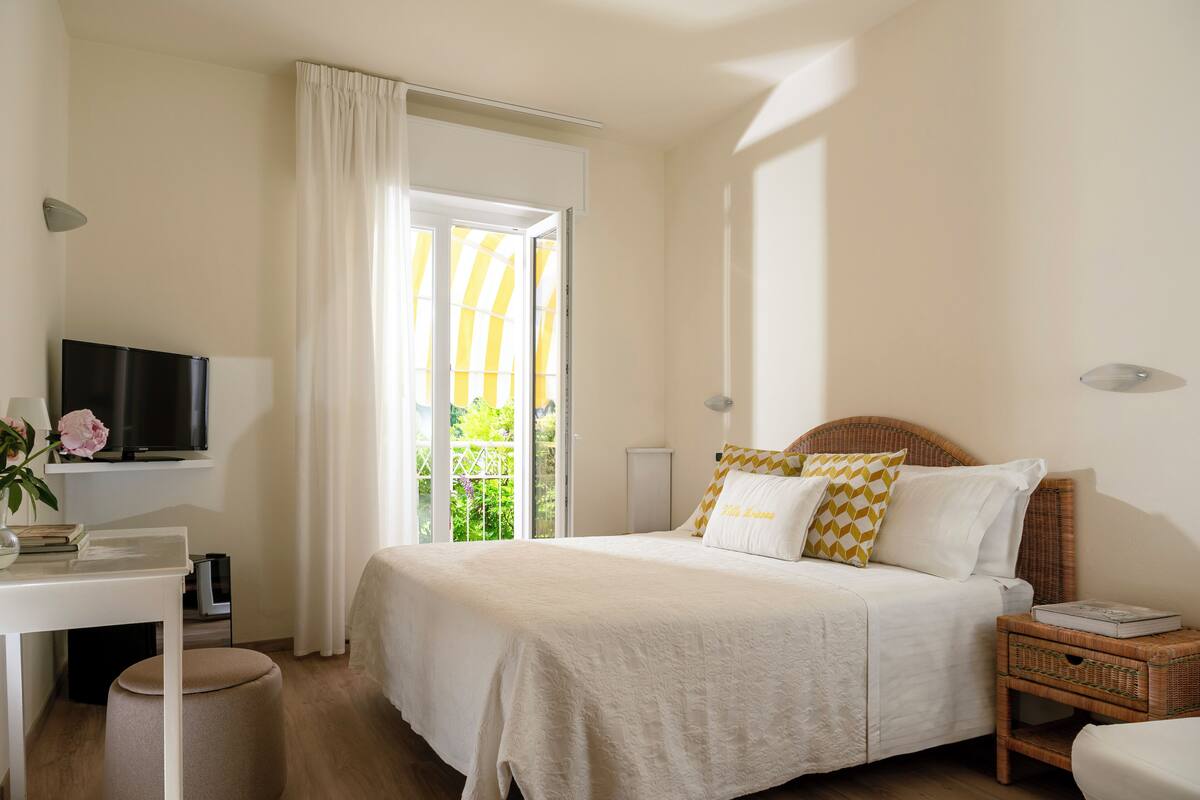 Une chambre à coucher avec un lit, un téléviseur posé sur un meuble, un bureau avec une chaise et une fenêtre avec des rideaux.