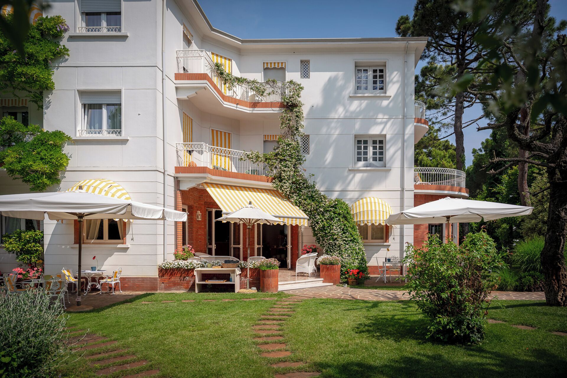 Ein mehrstöckiges Gebäude mit einer Terrassenanlage, ausgestattet mit Gartenmöbeln und Sonnenschirmen.