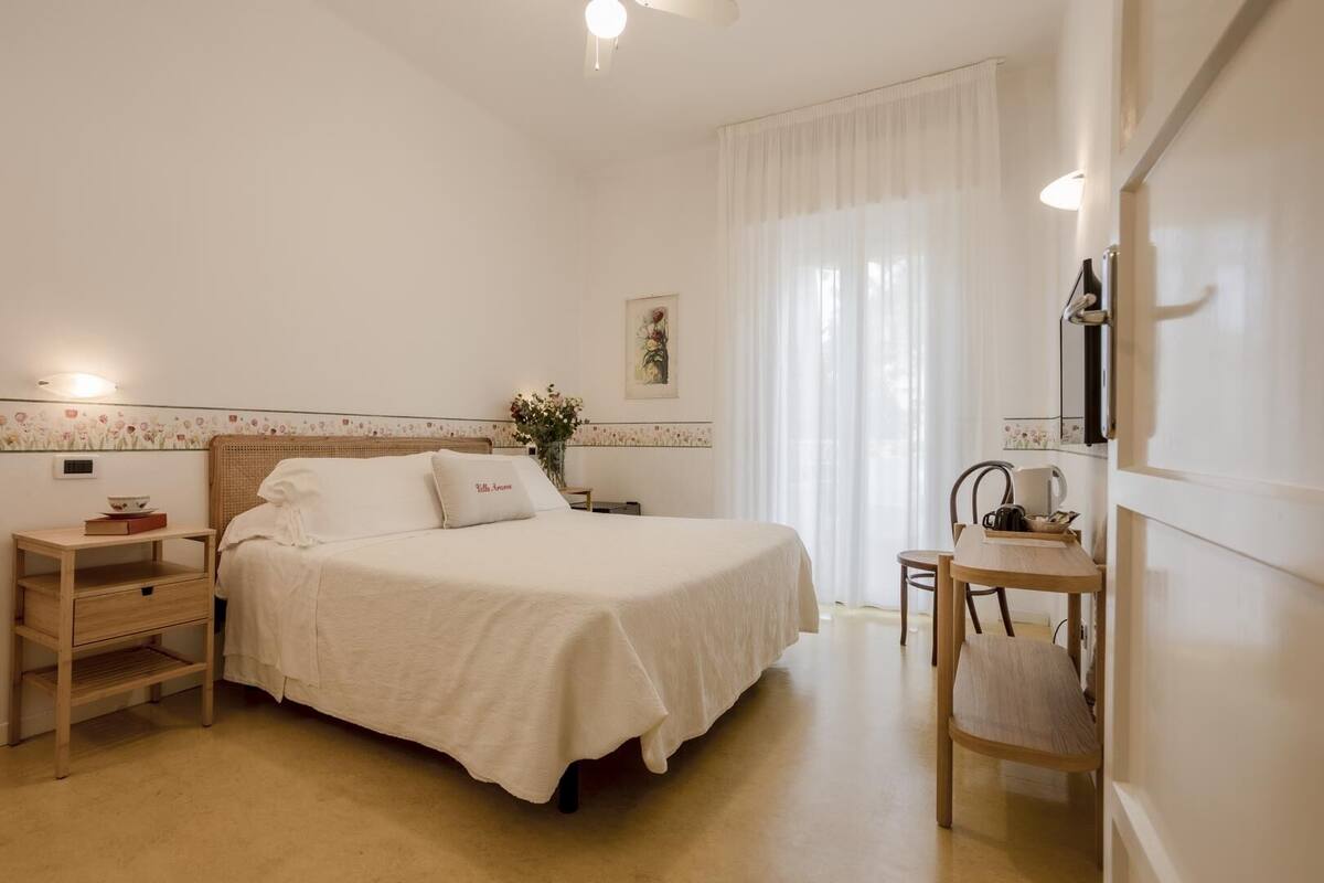 Une chambre d’hôtel bien rangée, avec un lit, une table de chevet, une chaise et un petit bureau avec une lampe.