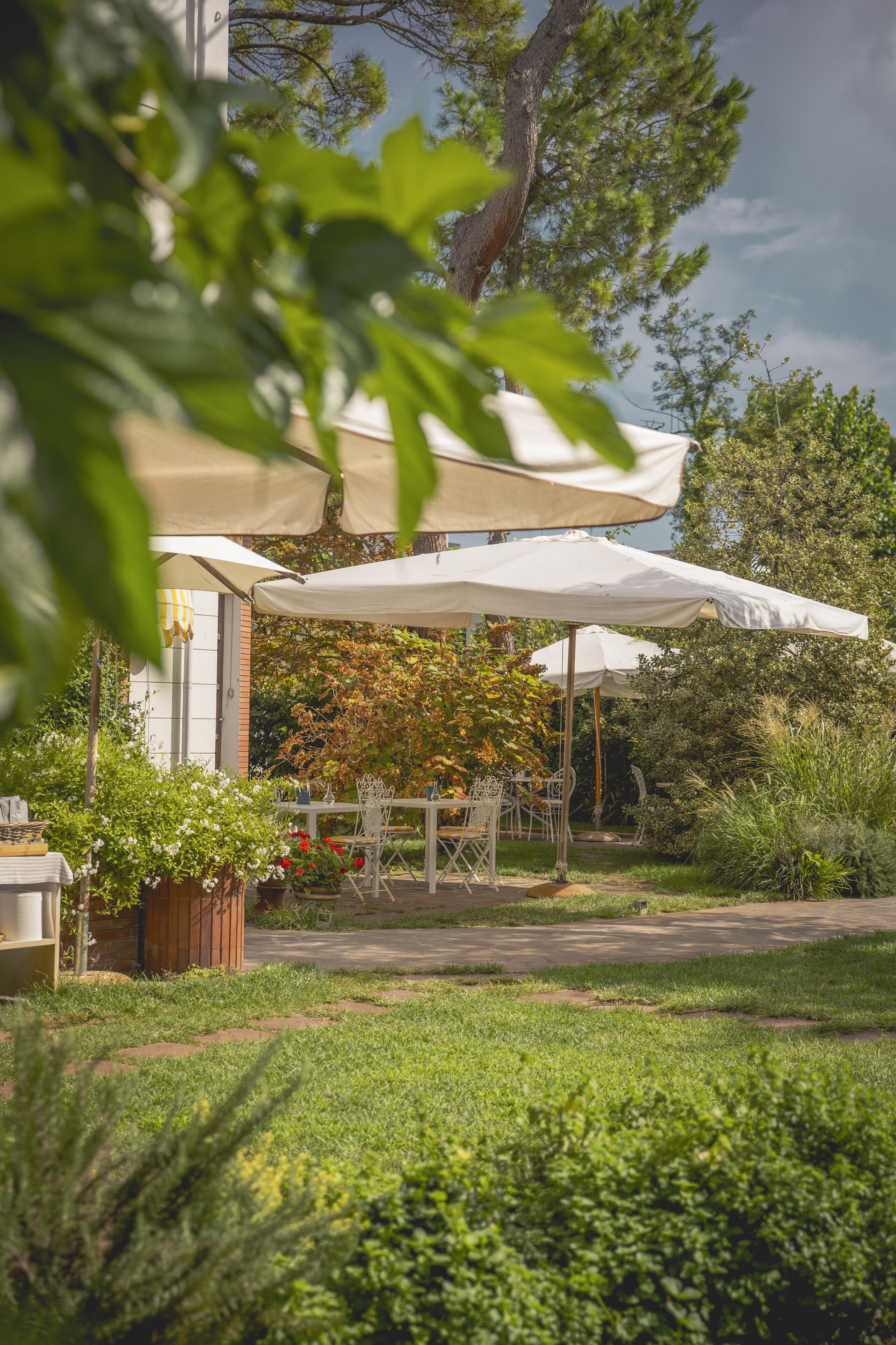 A patio area with outdoor seating under white umbrellas, surrounded by greenery and trees.