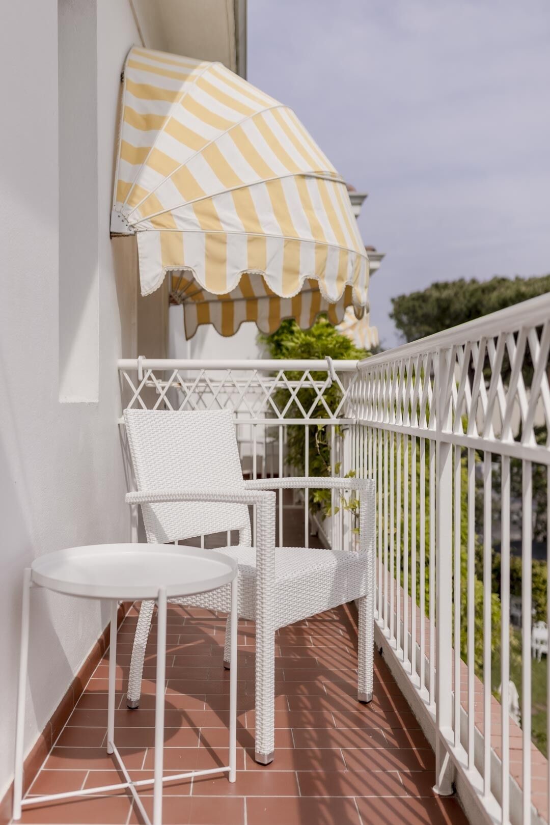 A balcony with a white chair and a small table, a striped umbrella, and a white railing.