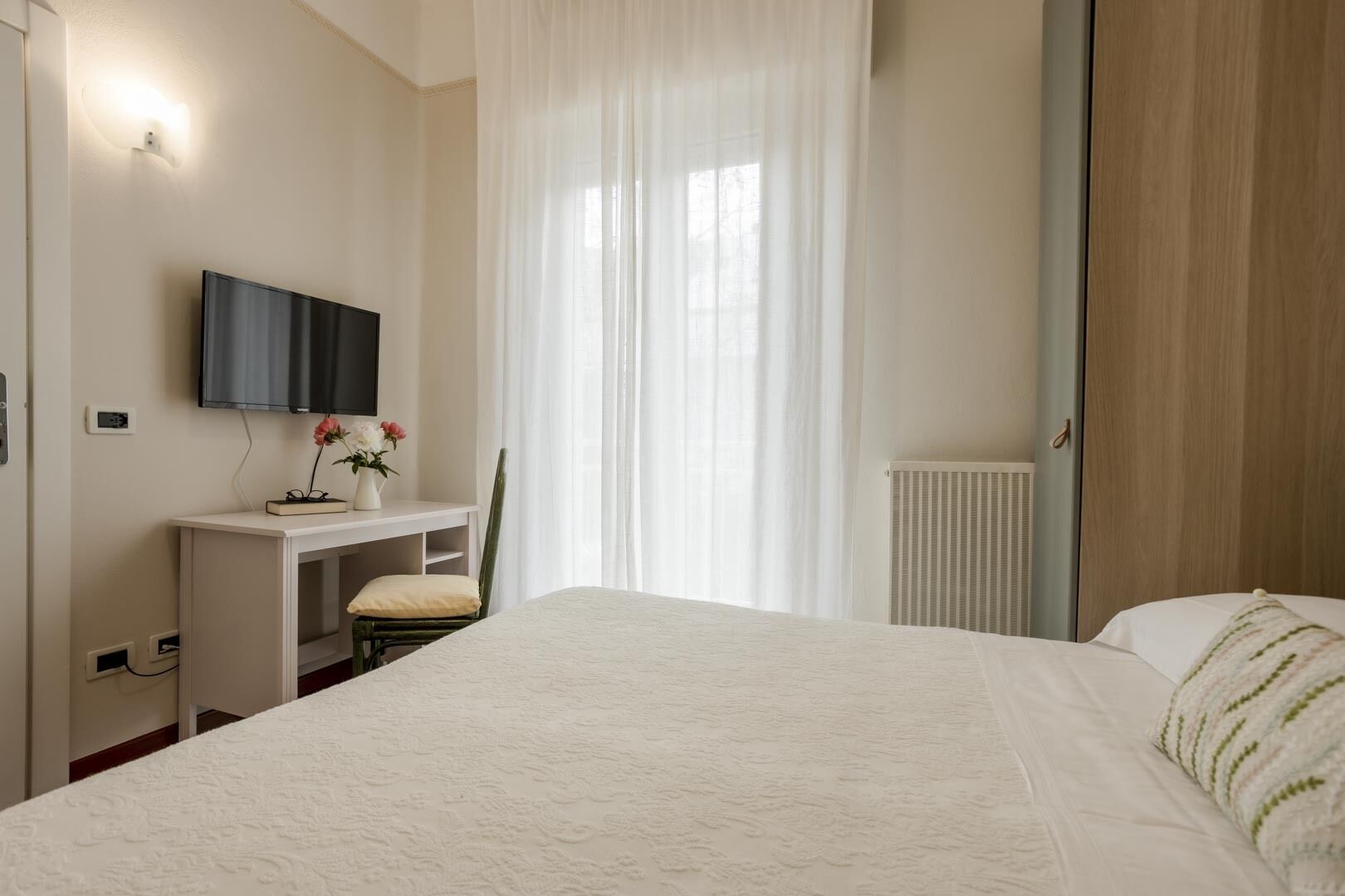 Un dormitorio con cama, escritorio, silla, televisor y radiador.