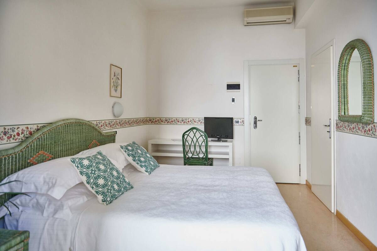 Une chambre à coucher comprenant un lit, un bureau avec un ordinateur, une chaise, une porte et un climatiseur fixé au mur.