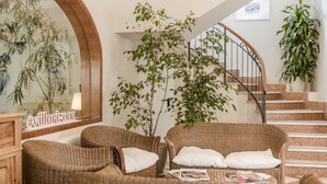 A cozy living area with wicker furniture, a staircase, and indoor plants. - Villa Arizona B&B (Cervia)