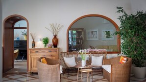 A living room with wicker furniture, a coffee table, and a large mirror. There are potted plants and a cabinet with decorative items. - Villa Arizona B&B (Cervia)