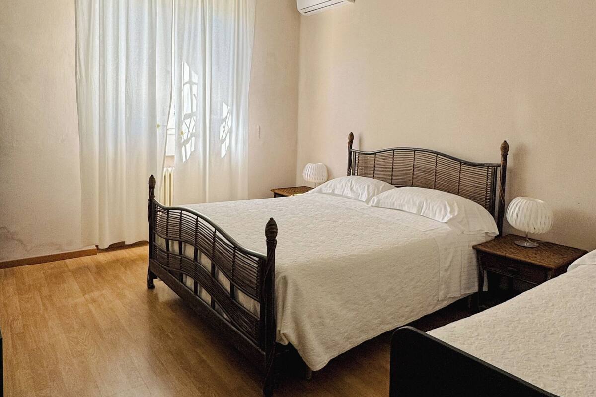 Une chambre avec un plancher en bois, un lit avec une tête de lit, un ventilateur de plafond et un appareil de climatisation.