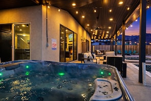 A hot tub with a warning sign, outdoor seating, and a view of the mountains. - Moab Desert Hideaway: 6-Bedroom Luxury Estate with Year-Round Pool & 2 Hot Tubs (Moab)