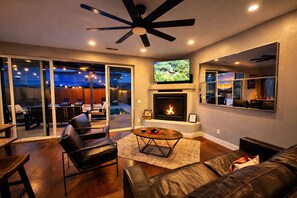 A modern living room with a fireplace, leather furniture, a ceiling fan, and a TV mounted on the wall. - Moab Desert Hideaway: 6-Bedroom Luxury Estate with Year-Round Pool & 2 Hot Tubs (Moab)