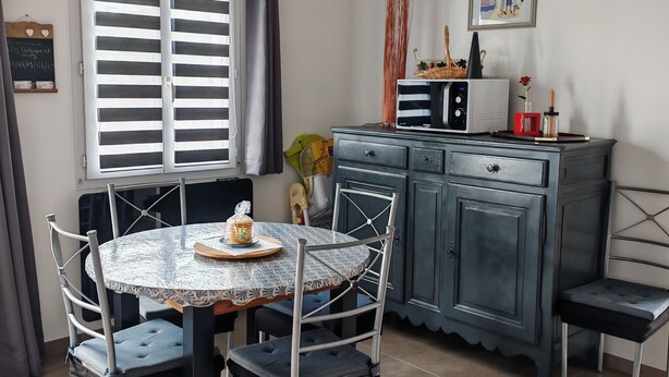 A dining area with a round table, chairs, and a cabinet. - LES Sables (Yves)