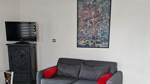 A living room with a grey sofa, a television on a cabinet, a large abstract painting on the wall, and a wicker chair. - LES Sables (Yves)