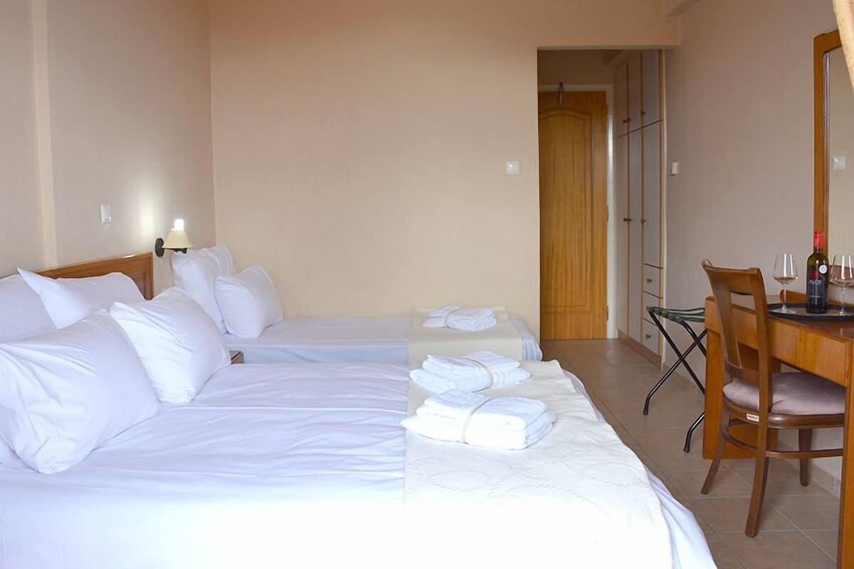 Ein Hotelzimmer mit zwei Einzelbetten, einem Schreibtisch mit Stuhl, einem Spiegel und einer Weinflasche.