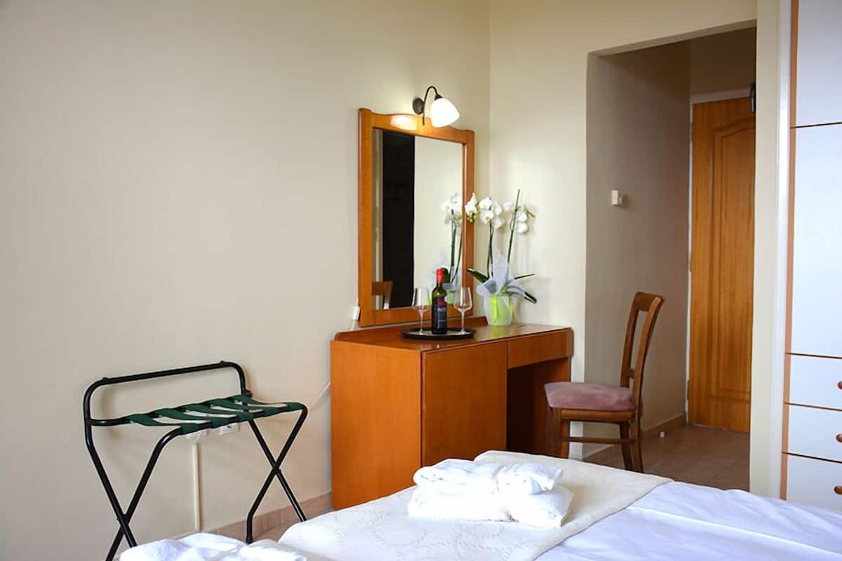 Ein Hotelzimmer mit einem Bett, einem Holztisch, einem Stuhl, einem Spiegel und einem kleinen Tisch mit Blumen in einer Vase.