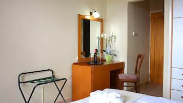 A hotel room with a bed, a wooden desk, a chair, a mirror, and a small table with a vase of flowers.
