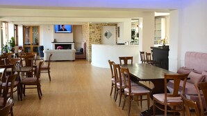 Un comedor espacioso con una mesa larga y varias sillas, una chimenea y un televisor montado en la pared.