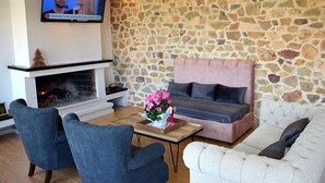 Una sala de estar con pared de piedra, una chimenea, un sofá rosa, un sofá blanco y dos sillones azules.