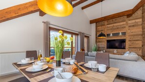 A dining area with a wooden table set for breakfast, a sofa, and a TV mounted on a wooden wall. - Appartement Ouréa 8 pers navette stations à 100m (Saint-Jean-de-Sixt)