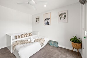 A bedroom with a white bed, a ceiling fan, and three framed wall art pieces.