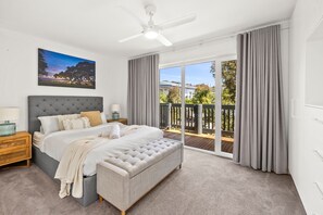 A bedroom with a large bed, a nightstand, a ceiling fan, and a view of the outdoors through a sliding glass door.