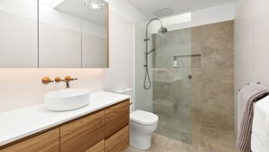 Een moderne badkamer met een wit wastafel, houten wastafelmeubel, een glazen douchecabine en een wit toilet.